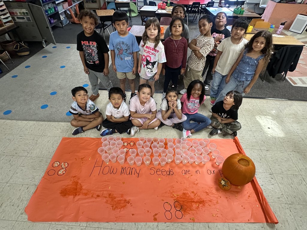 The class gathered behind the pumpkin activity poster, displaying rows of filled cups and the pumpkin on one side.