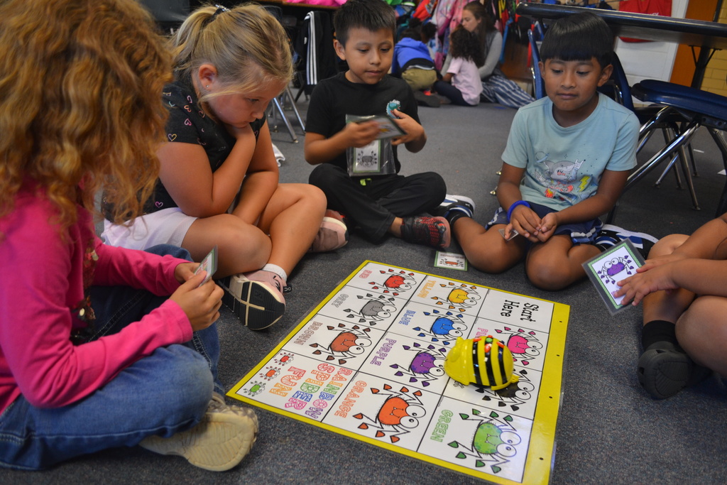 A group of students sits on their classroom floor using a Beebot.