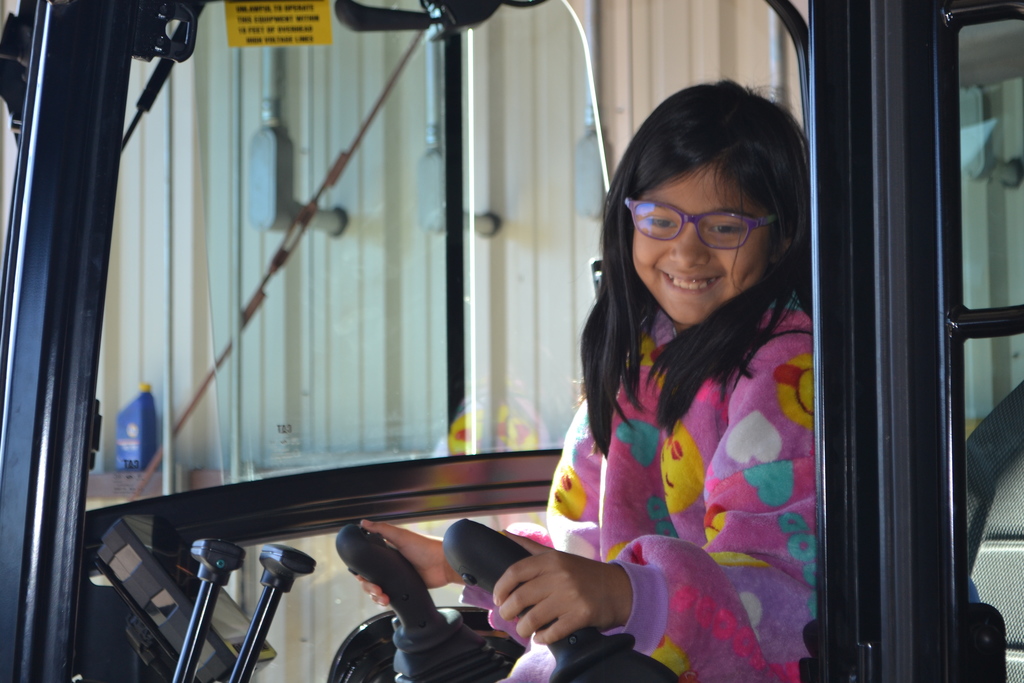 Image contains student smiling while pretending to drive a piece of operator equipment.