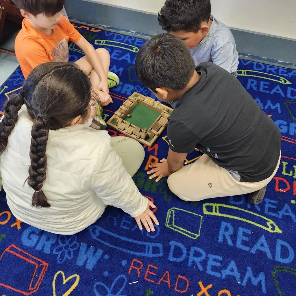 Four children sitting on a colorful classroom carpet playing with wooden blocks.