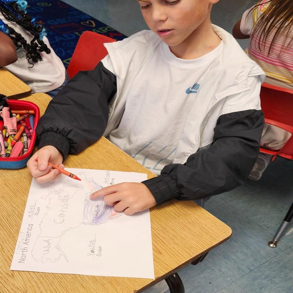 A student coloring a map of North America at their desk with crayons.