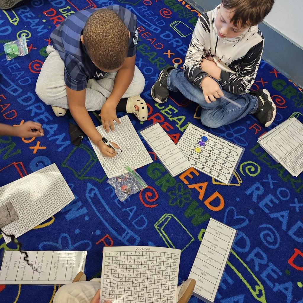 Students on the carpet using a 200 chart and counters for a math game.