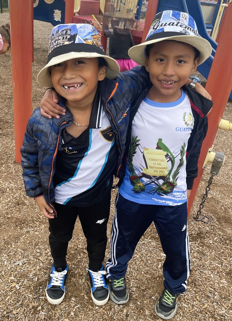 Two friends in matching hats pose on the playground with smiles on their faces. Hat reads Guatemala