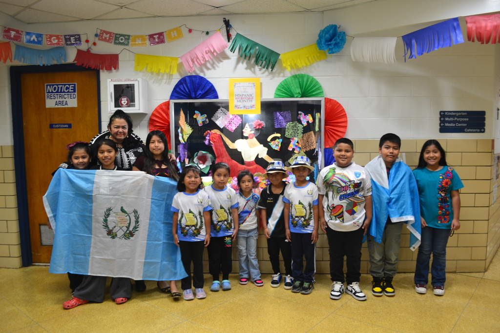 A large group of students in Hispanic Heritage spirit day clothing pose in front of the showcase decorated with bright colors and papel picado.