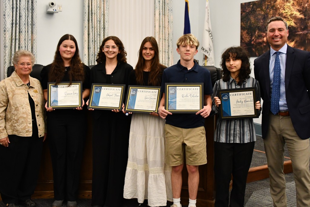 Five students holdnig certificates in a board room with a board member on the left and Principal on the right