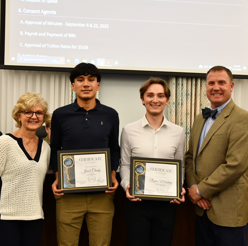 Two students holding certificates in board room with board member and principal