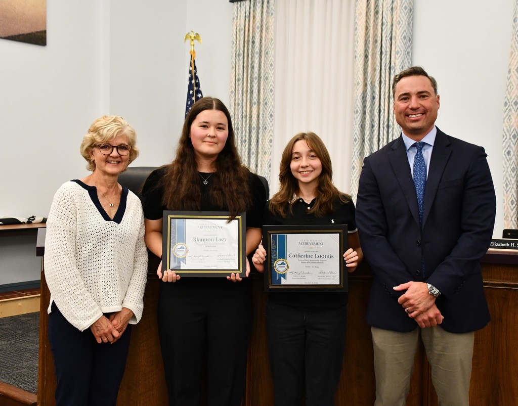Two students holding certificates in board room with board member and principal