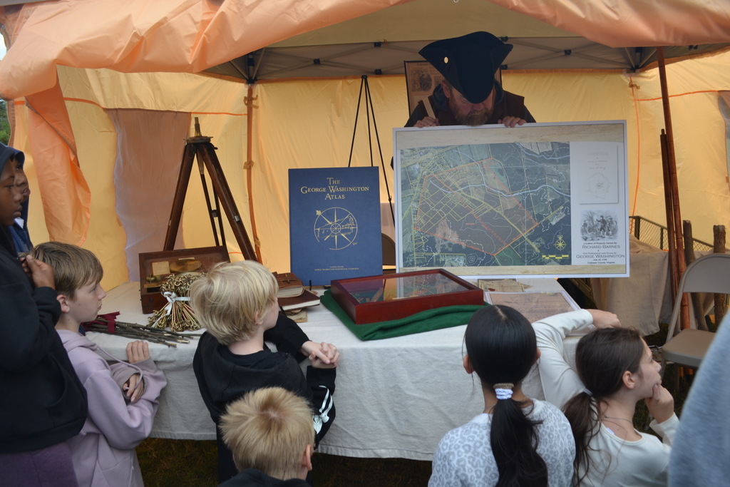 A colonial dressed man shows pieces of the surveying done by George Washington in a tent in the park.
