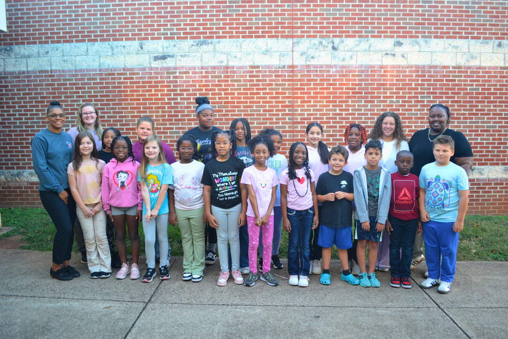Image contains two rows of students and 4 adults posing in front of a brick wall.