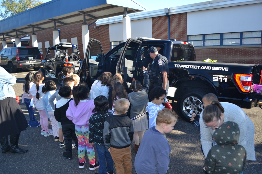 A group of kids is outside the front of the school looking at a police truck  To PROTECT AND SERVE