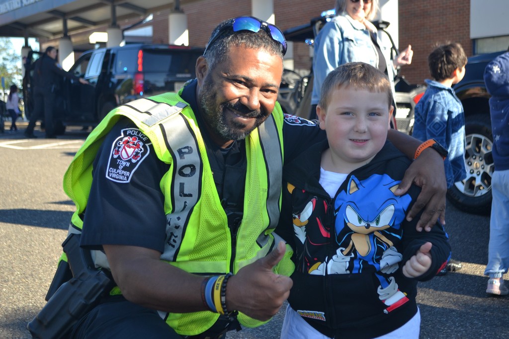 A police officer in a bright vest bends down next to a student in a  Sonic hedgehog jacket to give a thumbs up to the camera.