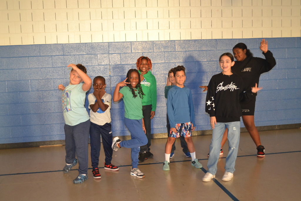 Image contains 8 students in the school gym posing happily for the camera in the school gym.