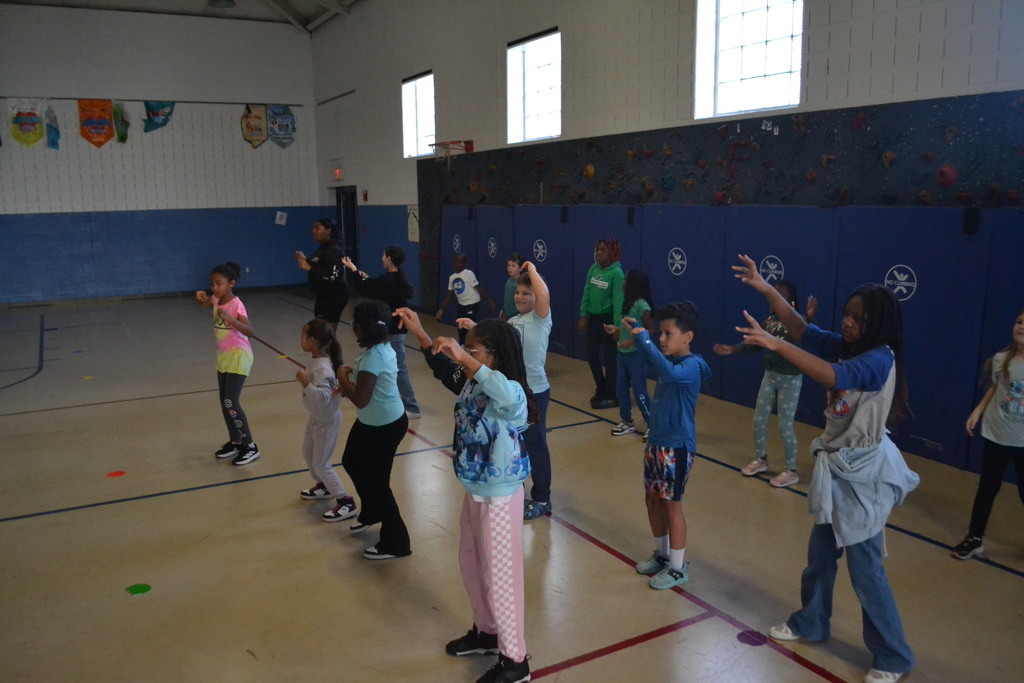 Image contains 3 rows of students dancing in sync in the school gym.