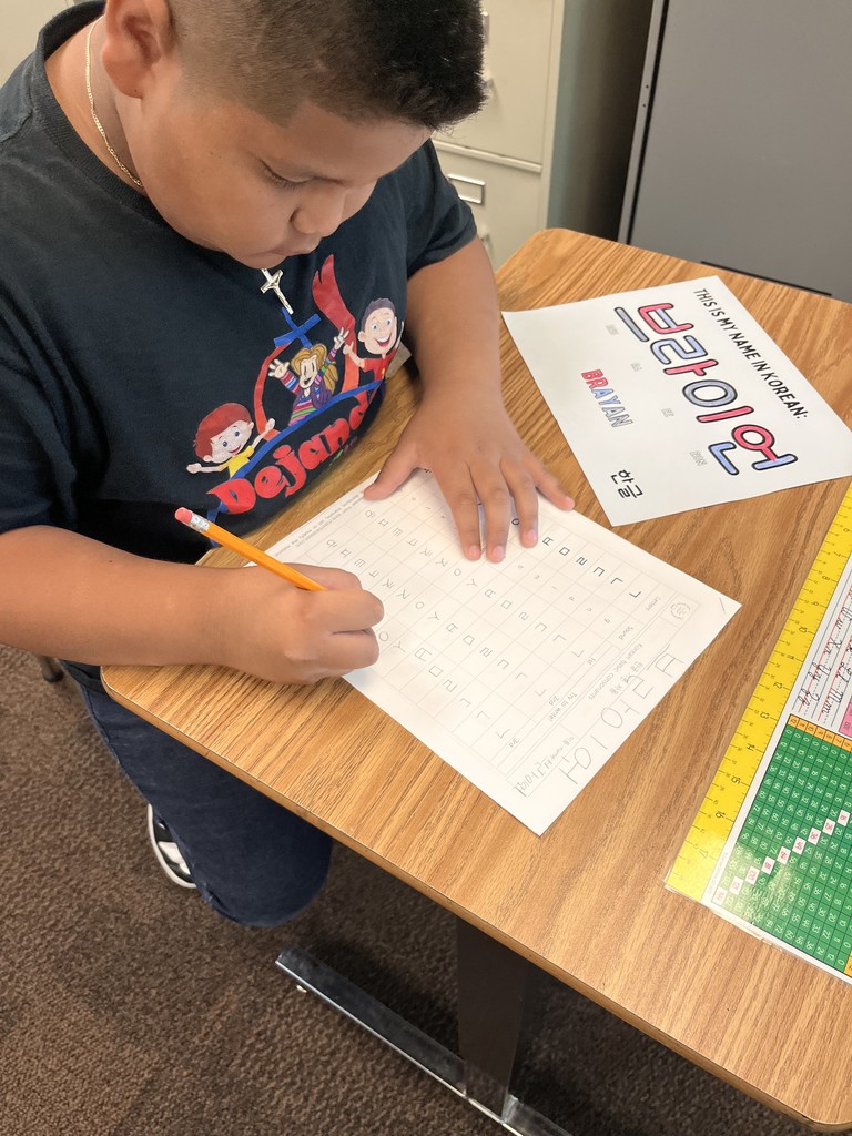 Image contains a boy at his desk working on a Korean alphabet sheet.