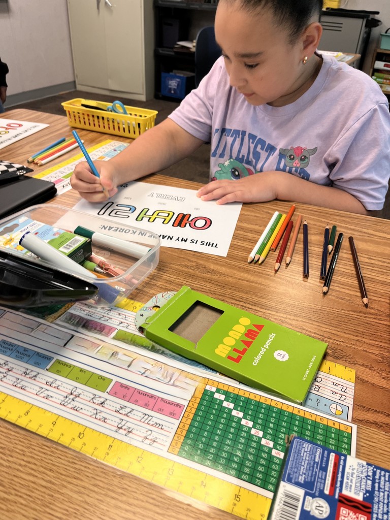 Image contains a girl at her desk working on coloring her name in the Korean alphabet.