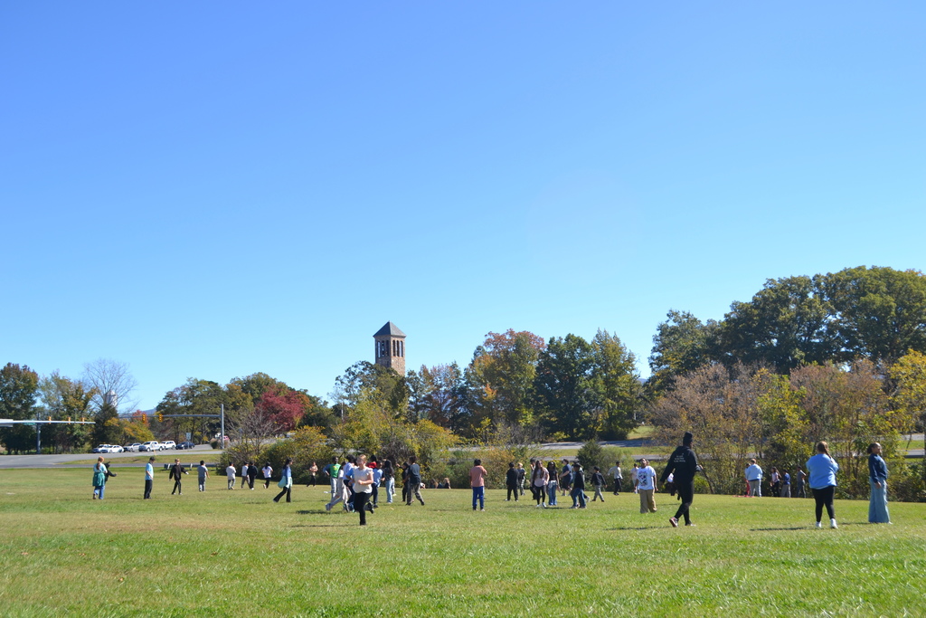 Image contains a group of kids playing in a grassy field with a bell tower in the far distance.