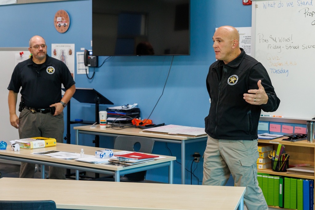 Two law enforcement officers speak to students in CTEC’s EMT classroom. One officer stands at the front of the room addressing the class while the other observes.