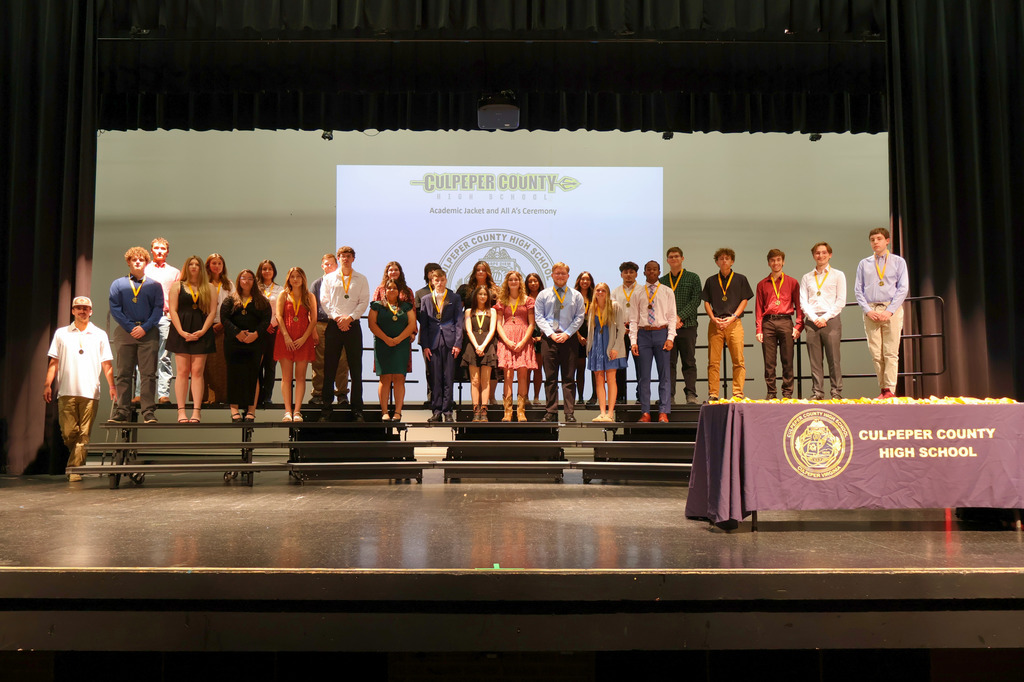 A large group of students stands on risers on a stage wearing medals around their necks during the Culpeper County High School Academic Jacket and All A’s Ceremony. A presentation slide with the school logo is projected behind them.
