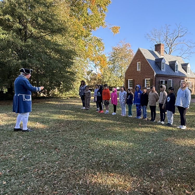 several young students are walking in in line on a grassy lawn outside a historic brick building