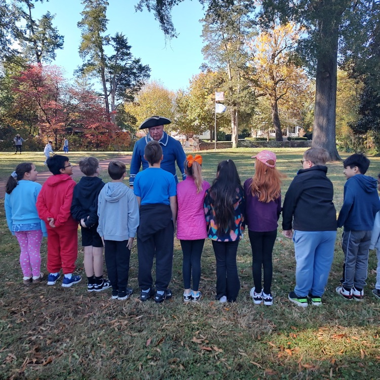 students in a line listening to a man dressed in colonial clothes 