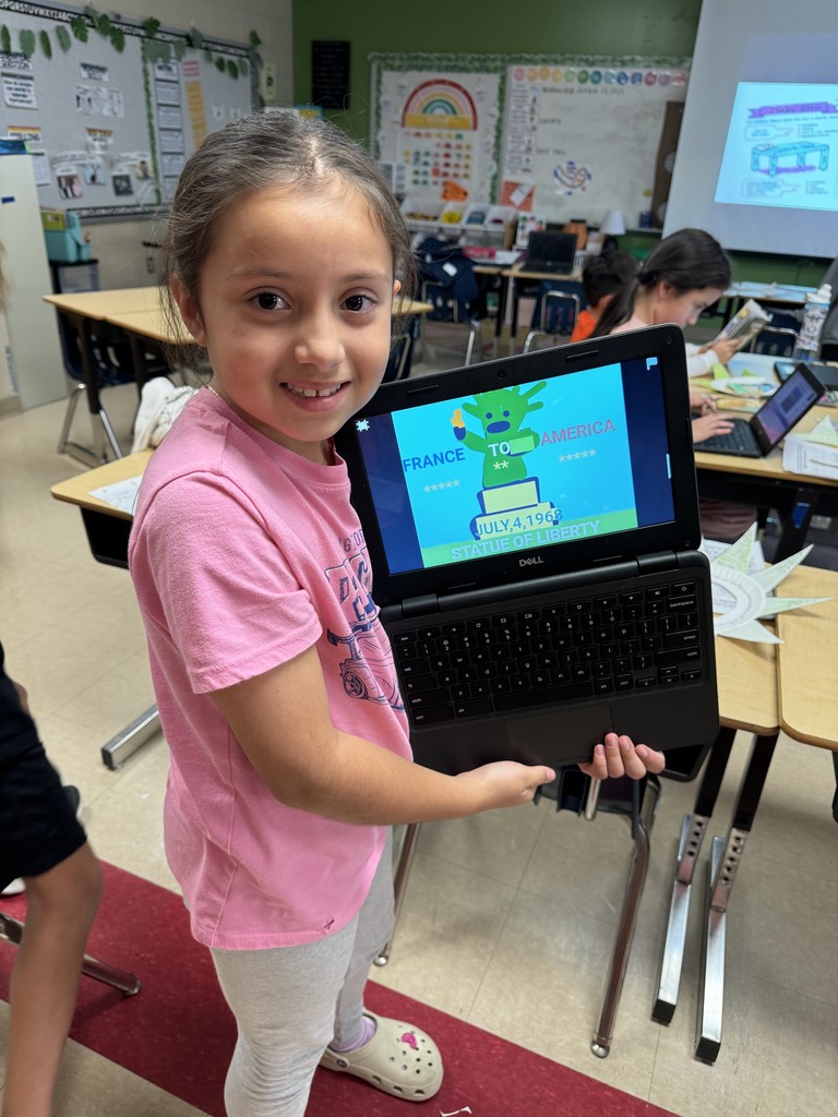 A student in a pink shirt holds a Chromebook displaying a colorful digital drawing of the Statue of Liberty labeled “France to America, July 4, 1886.”