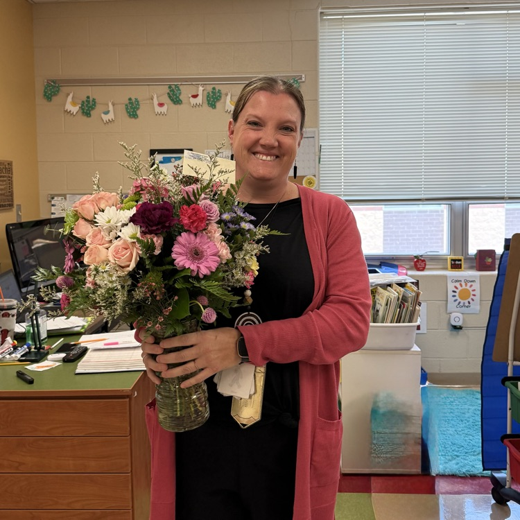 teacher, Erin Gomez smiles while posing for the camera and holding a bouquet of flowers