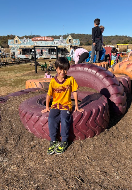 Photo 5: A boy in a Washington Commanders shirt sits on large purple tractor tires with the farm’s “Haunted House” attraction in the background.