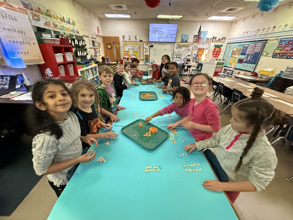 A wider view of the classroom showing a larger group of students sitting at multiple tables, all engaged in the same activity, likely involving counting.