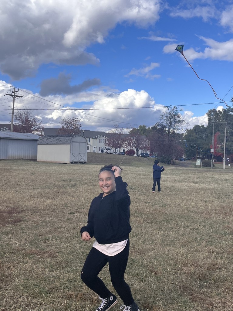 Girl flying a kite in a field with a smile on her face.
