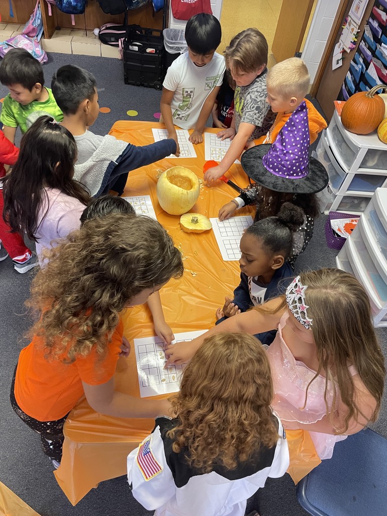1st graders do pumpkin math around a table with an orange table cloth.