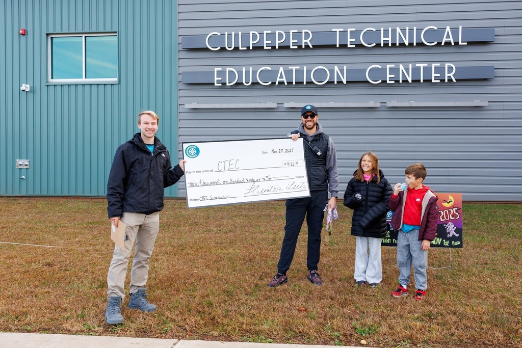 Two event organizers hold a large check for $9,166.00 made out to CTEC for scholarships, standing in front of the Culpeper Technical Education Center sign.