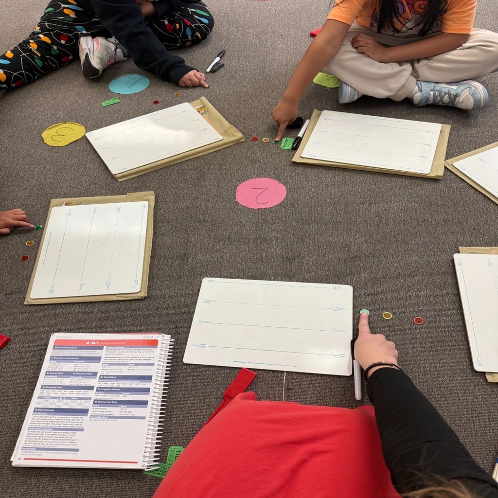 Elementary students work together on a phonics activity, using magnetic letters and whiteboards arranged in a circle.