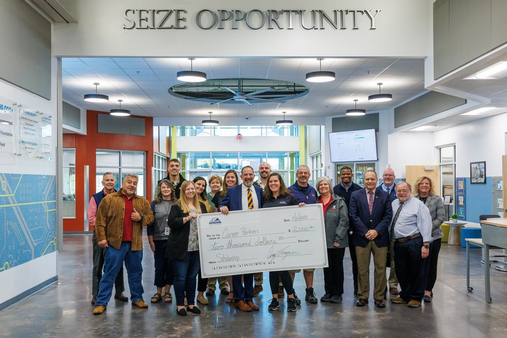 A large group of people pose together inside the Culpeper Technical Education Center under the “Seize Opportunity” sign, holding a $2,000 check made out to Career Partners for scholarships.