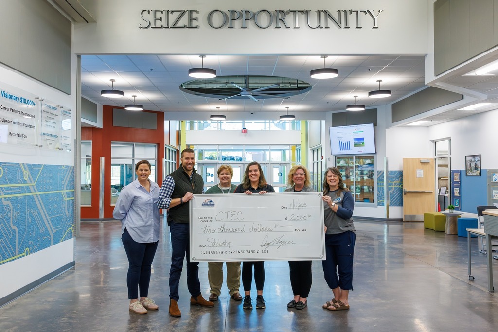 Six people stand inside the Culpeper Technical Education Center under the “Seize Opportunity” sign, holding a large check for $2,000 made out to CTEC for scholarships.