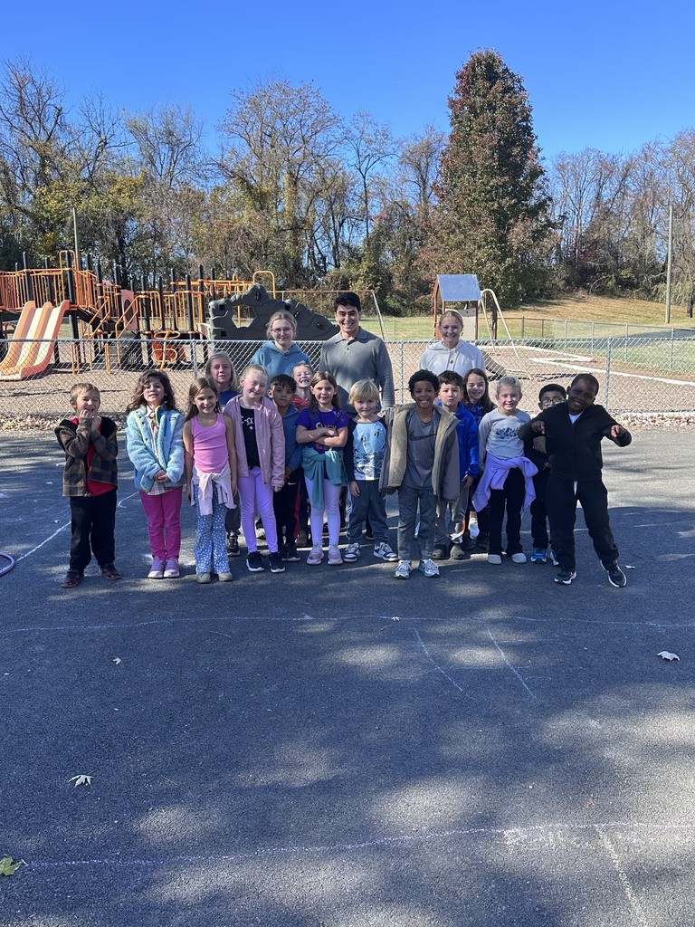 A large group of children and adults posing together for a class or team photo outdoors.