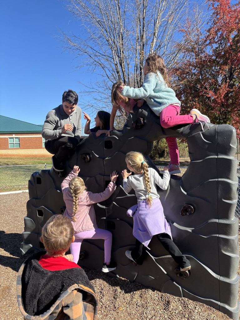 Several children sitting and playing on a large, gray climbing structure under a blue sky.