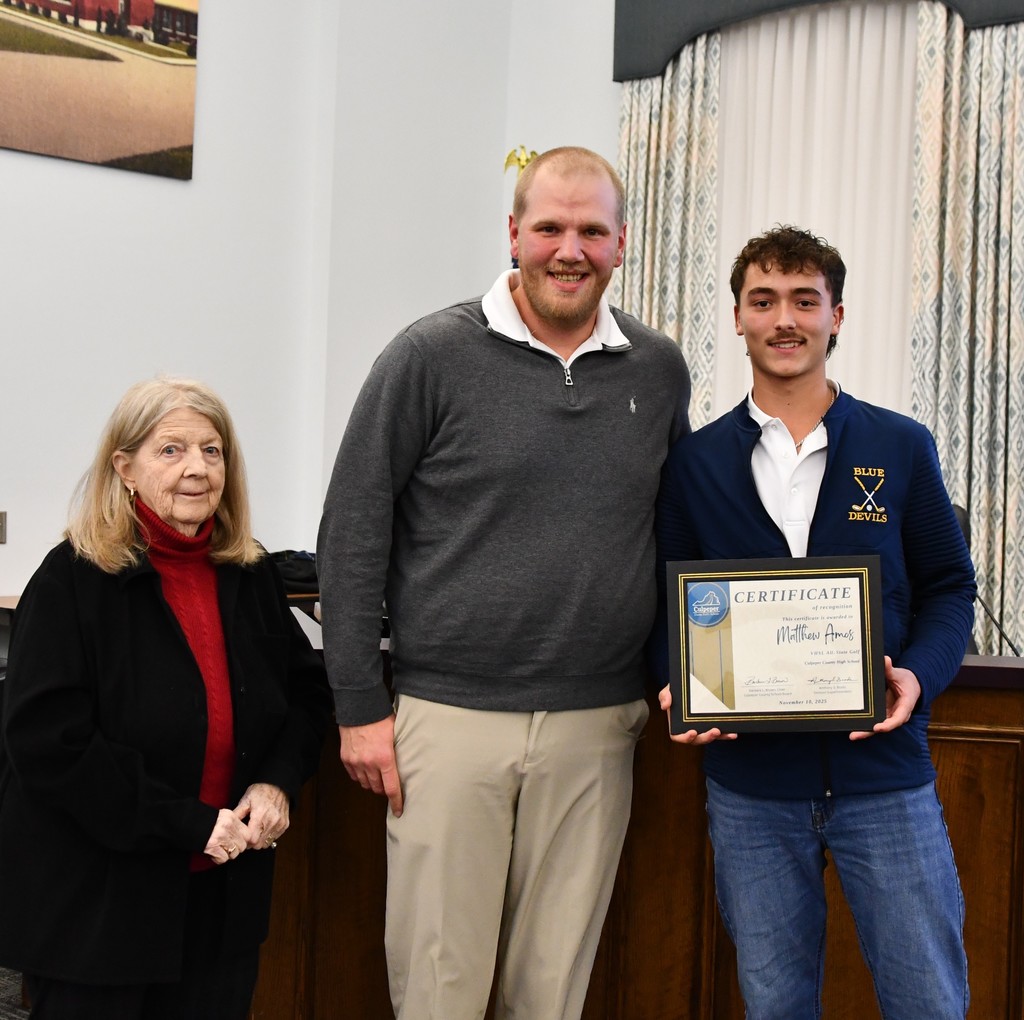 student standing in board room holding certificate with very tall coach in the middle and board member on the left