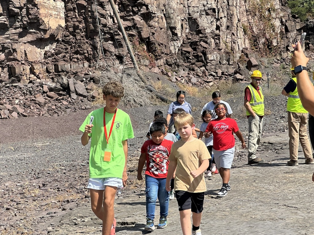 “Children and adults walking together in a rock quarry; a student leader in a green shirt and safety workers in hard hats are visible.”