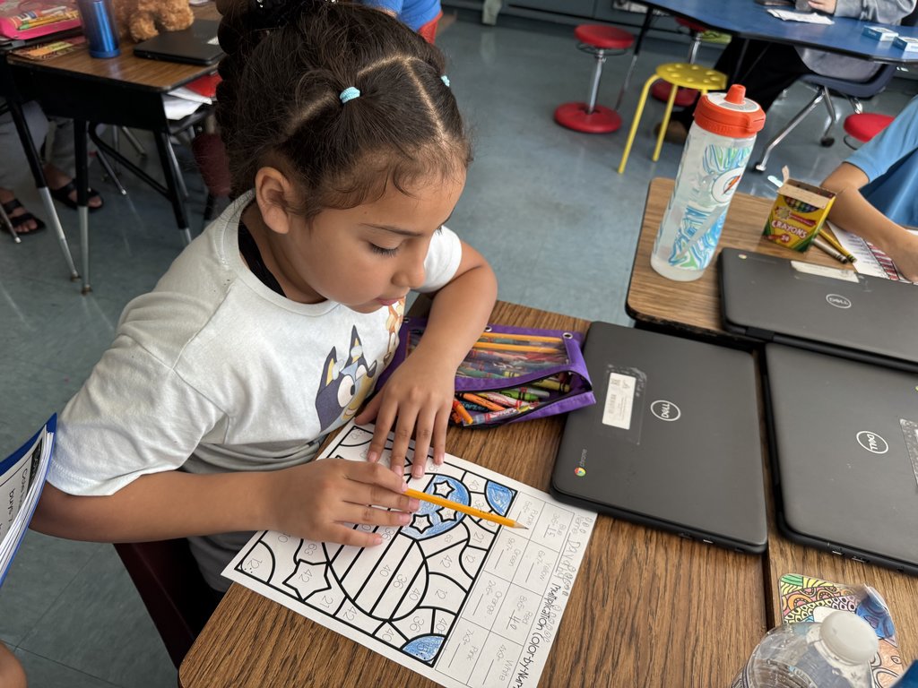 “Student focused on coloring a math worksheet at a desk with school supplies and Chromebooks around.”