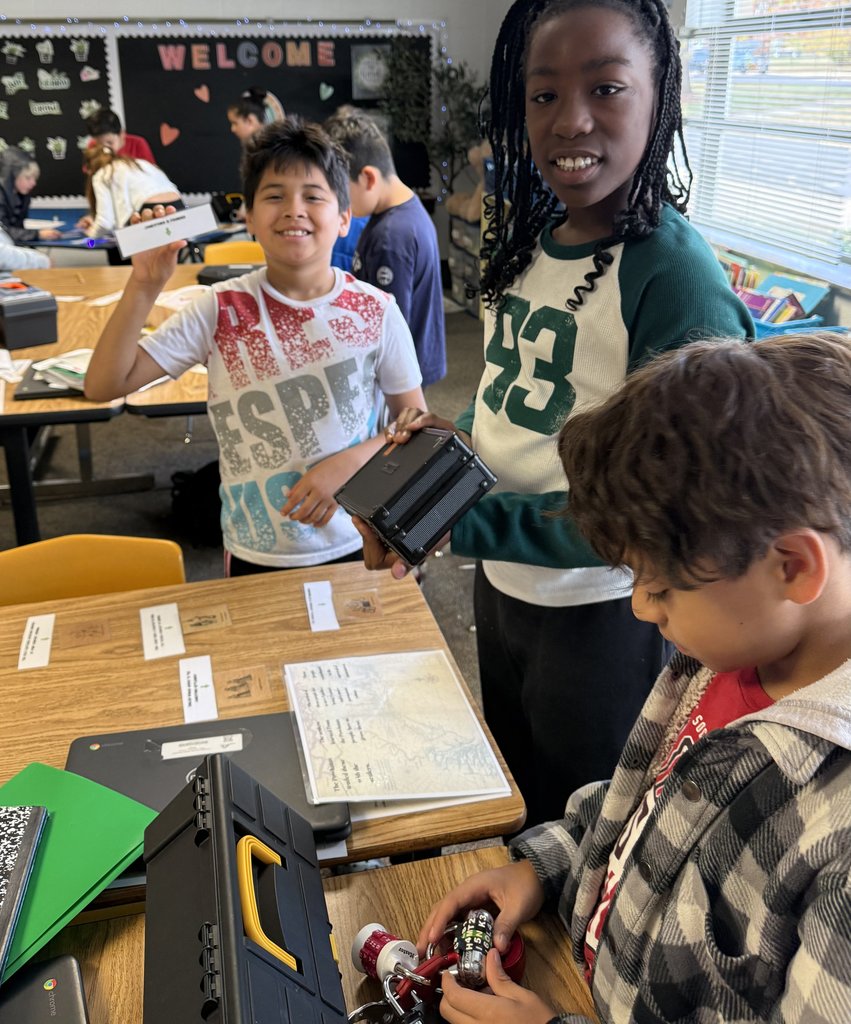 “Students smiling and holding lockboxes while participating in a classroom breakout activity with maps and notebooks on the table.”