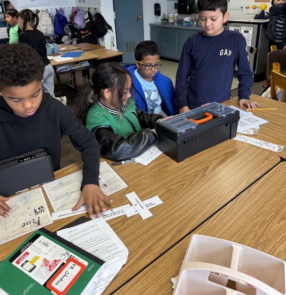 “Students at a table working together on papers and a black lockbox during a classroom breakout challenge.”
