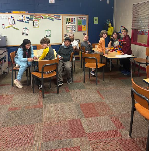 everal groups of students sit at tables around the classroom, working on puzzles and clues. They are spread out across the room, chatting and collaborating.
