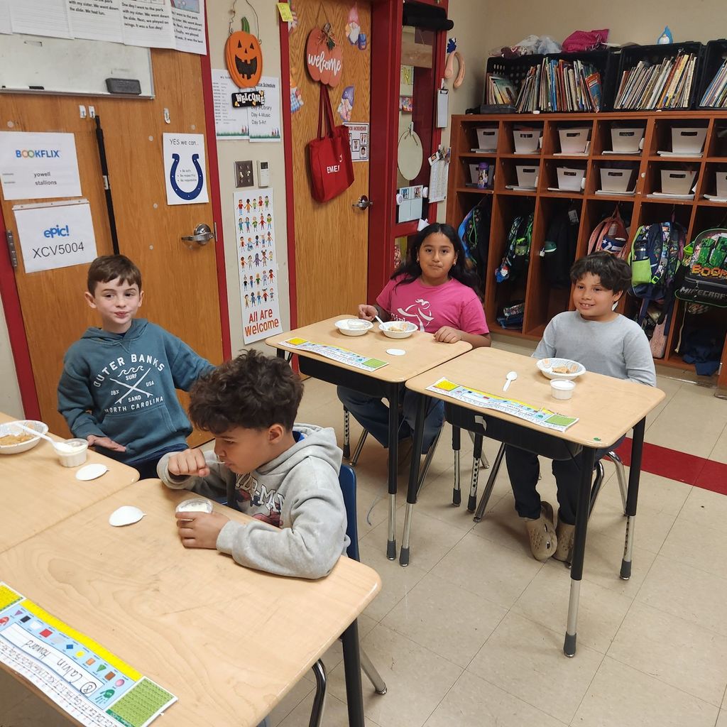 Another group of students sit at desks, smiling and eating apple pie and ice cream. Backpacks and cubbies line the wall behind them.
