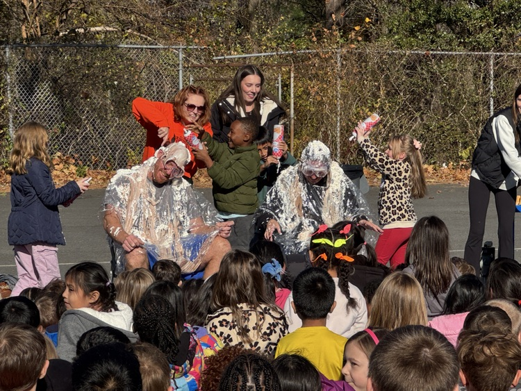 A group of students sitting and watching two people get covered in whipped cream and ice cream