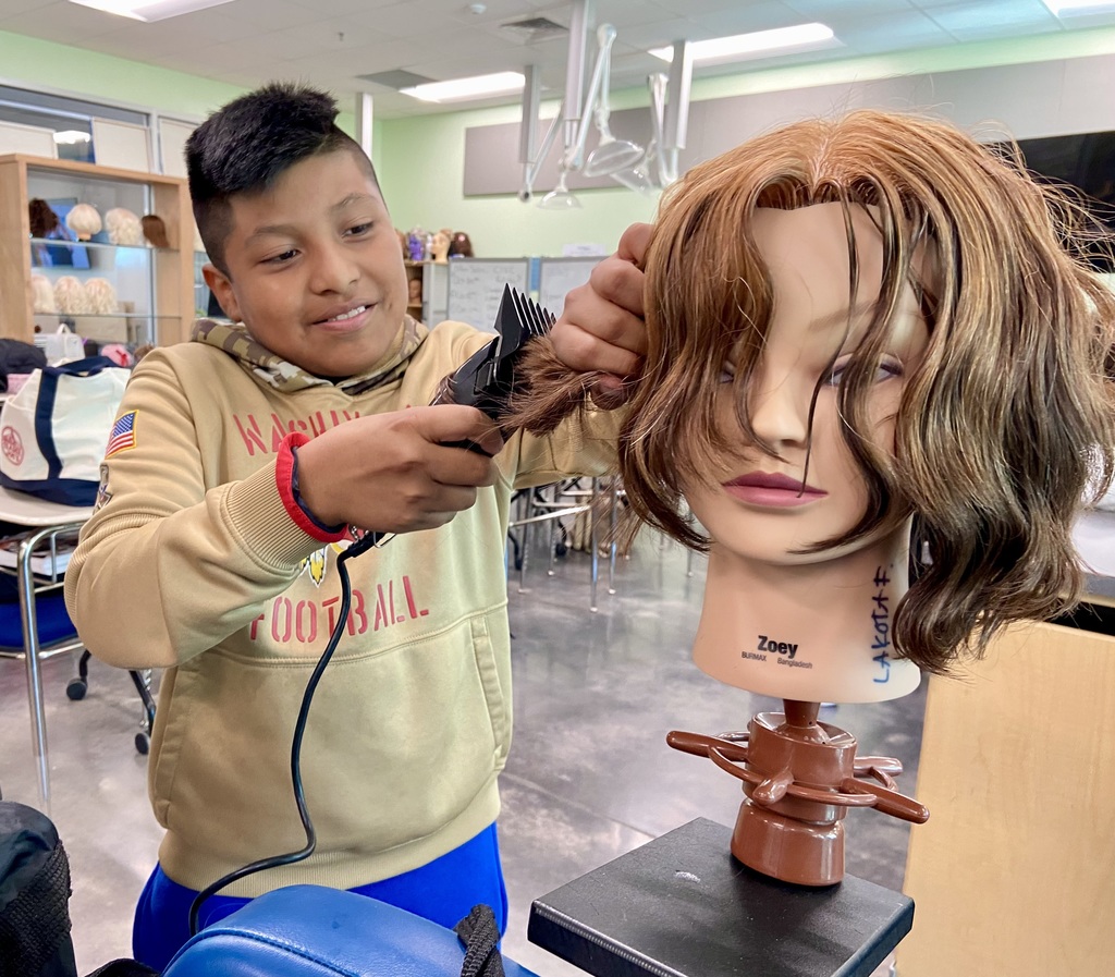 Student uses clippers on a head maniquin learning how to be a barber in an classroom.