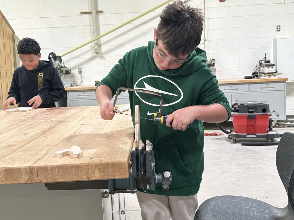 A student in a green sweatshirt cutting wood