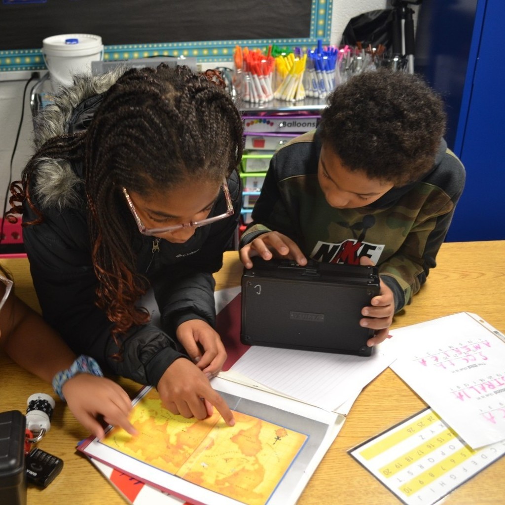 Two students work together in a classroom to use a map to get a code to open the lockbox.