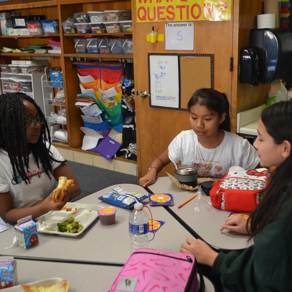 Three female students eat lunch in a classroom while playing Math 24.