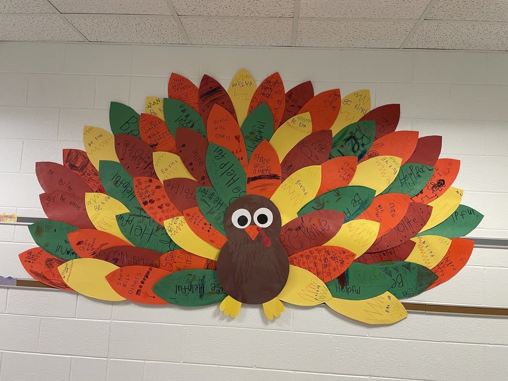 A colorful turkey made of construction paper is on the school wall. Each feather has a hand written note or picture from a kindergartners about why they are thankful.
