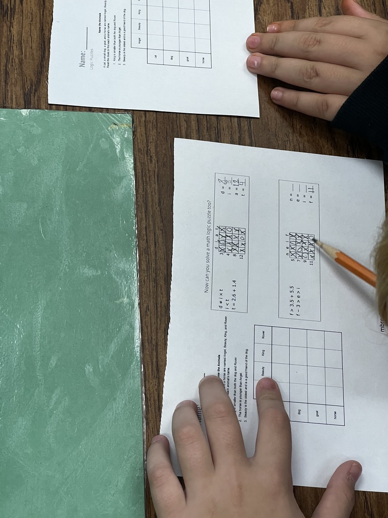 A math logic puzzle worksheet showing completed grid puzzles. The boxes contain X marks and filled-in circles, with student-written answers such as “d = 8,” “i = 3,” “a = 12,” and “t = 4.”